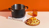 Meyer stainless steel stockpot and a plate of cheese fries and a glass cup arranged against a bold orange background