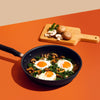 Accent nonstick skillet with fried eggs alongside a wooden cutting board and ingredients